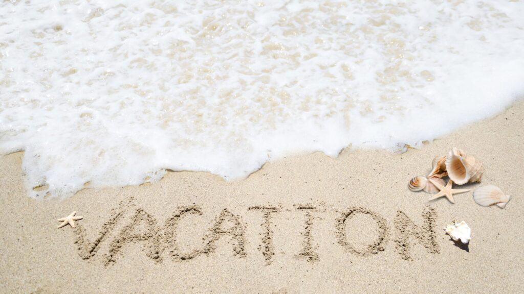 wave landing on beach, vacation written in sand