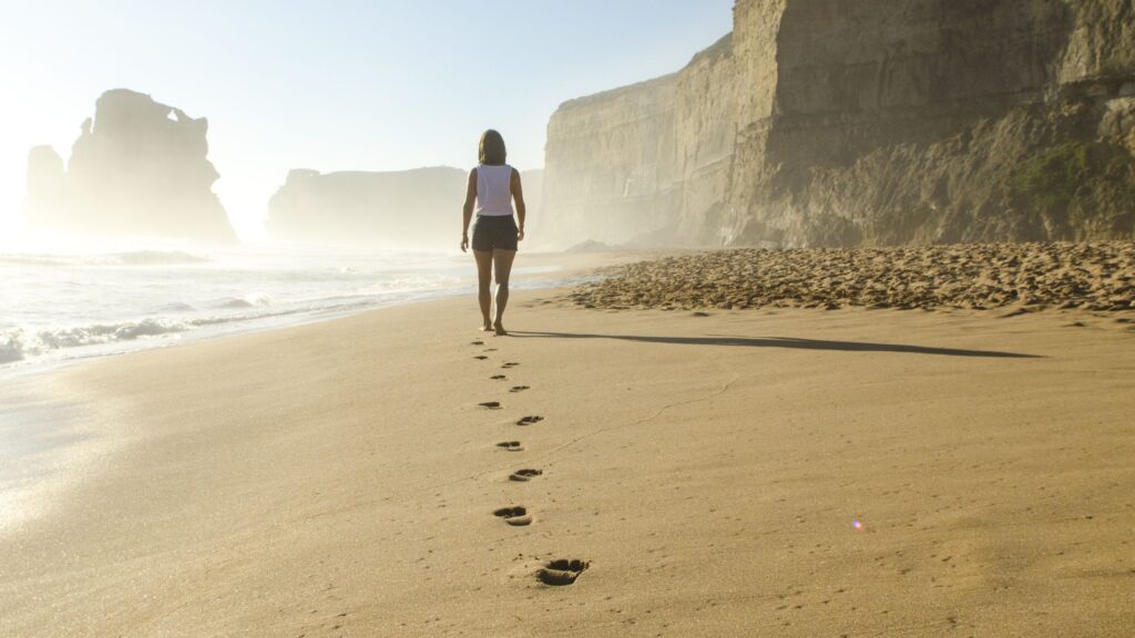 Woman walking along beach leaving footprints in the sand.