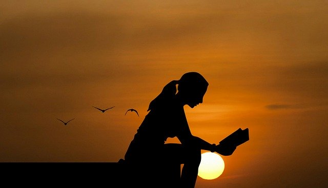 A woman reading a book peacefully as the sun sets