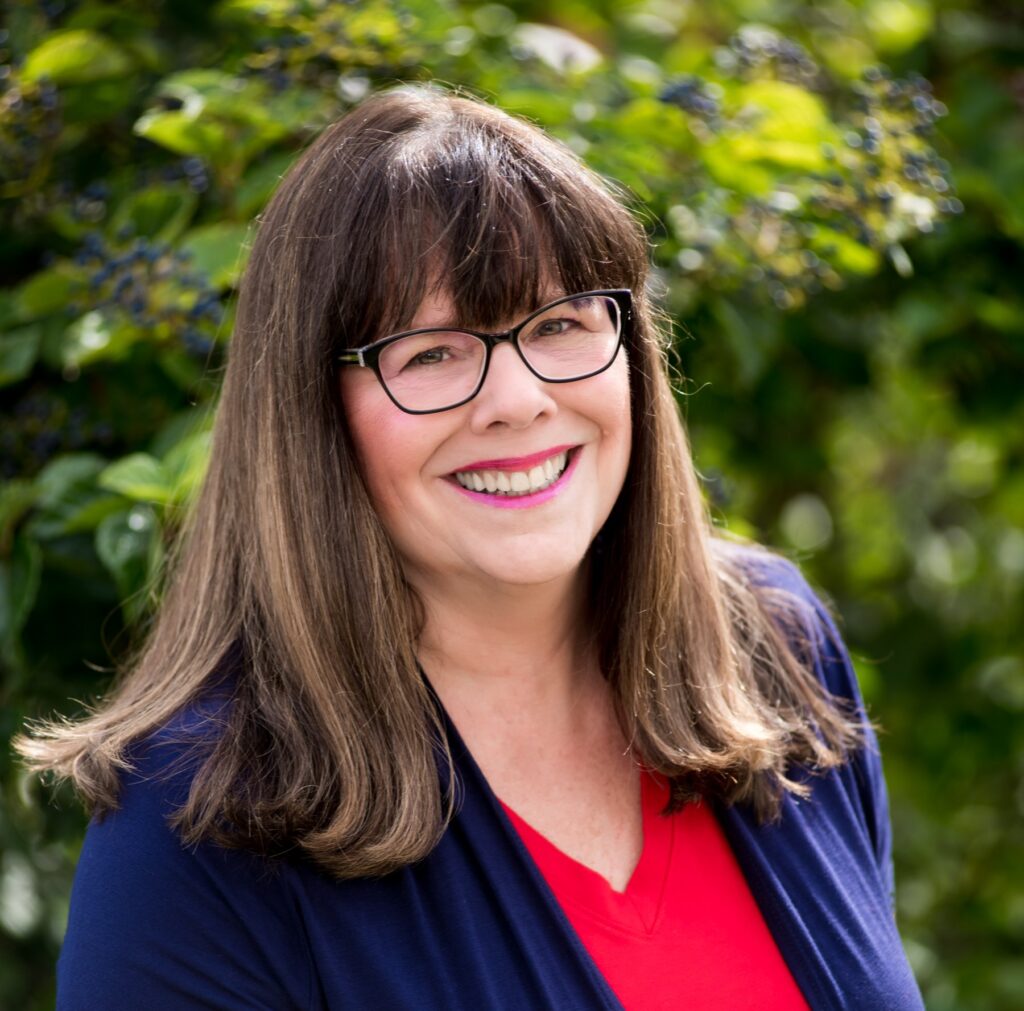 picture of author Corinne Kelli showing shoulder length brown hair and glasses.